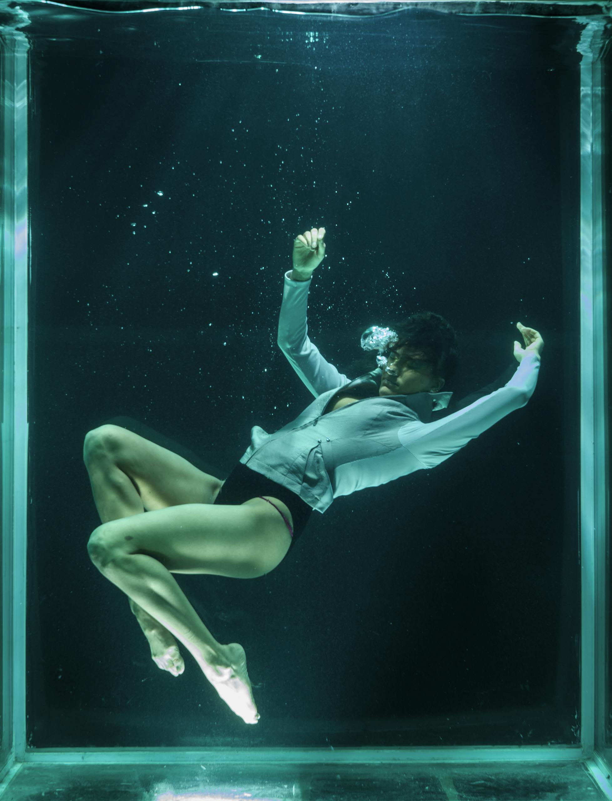 Artistic underwater photoshoot capturing a woman gracefully posed in a submerged tank.